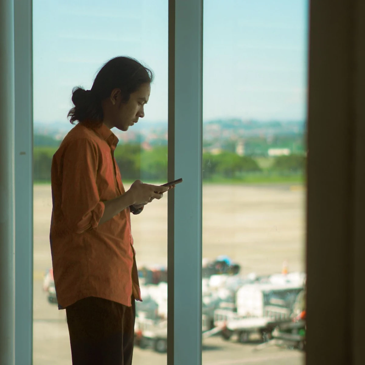 A traveller checking a phone by an airport window