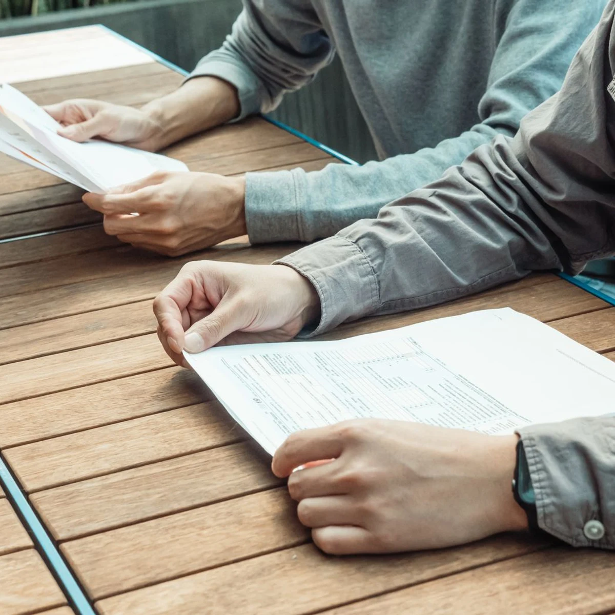 Two people reading printed documents across a wooden table