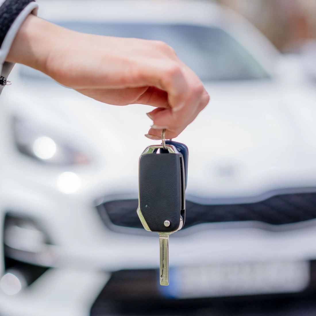 A hand holding a car key in front of a white car