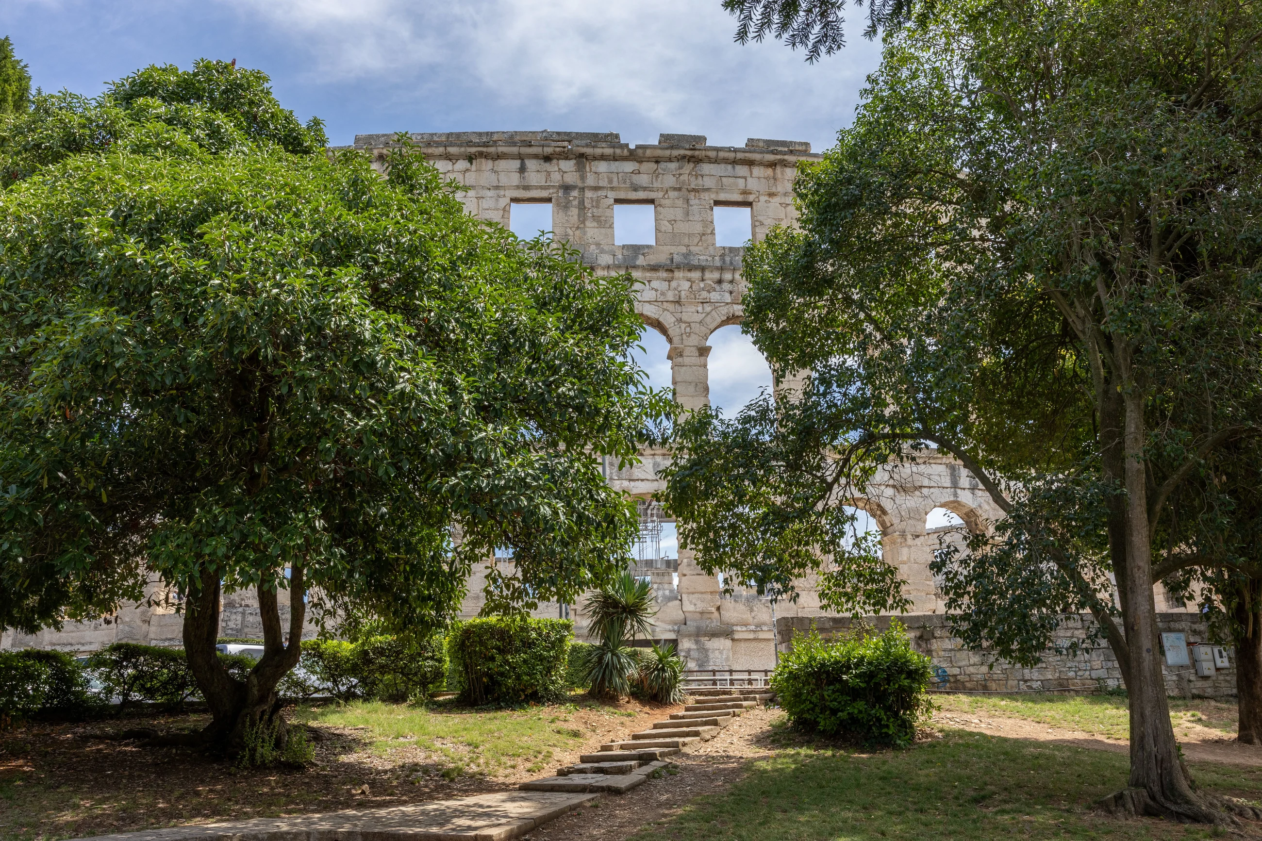 The walls of the Roman amphitheatre in Pula behind trees