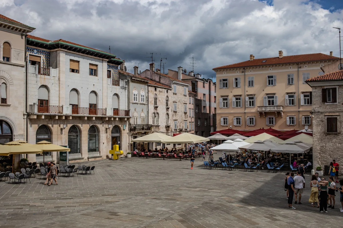 A square in Pula old town with cafe tables under parasols