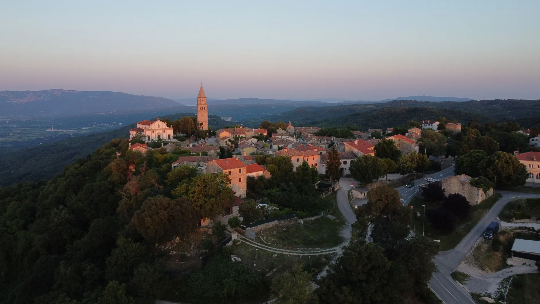 A hilltop village in Istria at sunset, with a bell tower and a road curving below