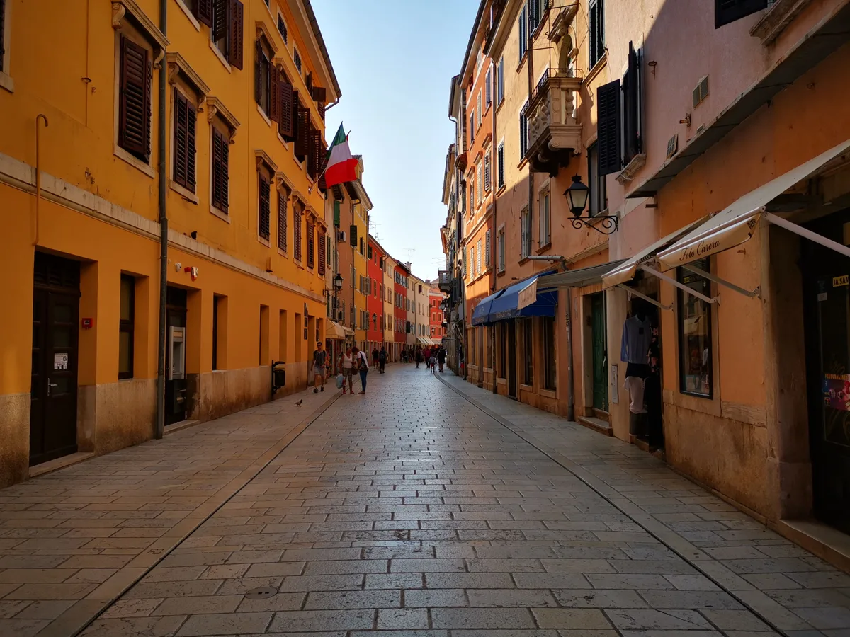 A paved pedestrian street in Rovinj lined with orange and pink buildings and shop awnings