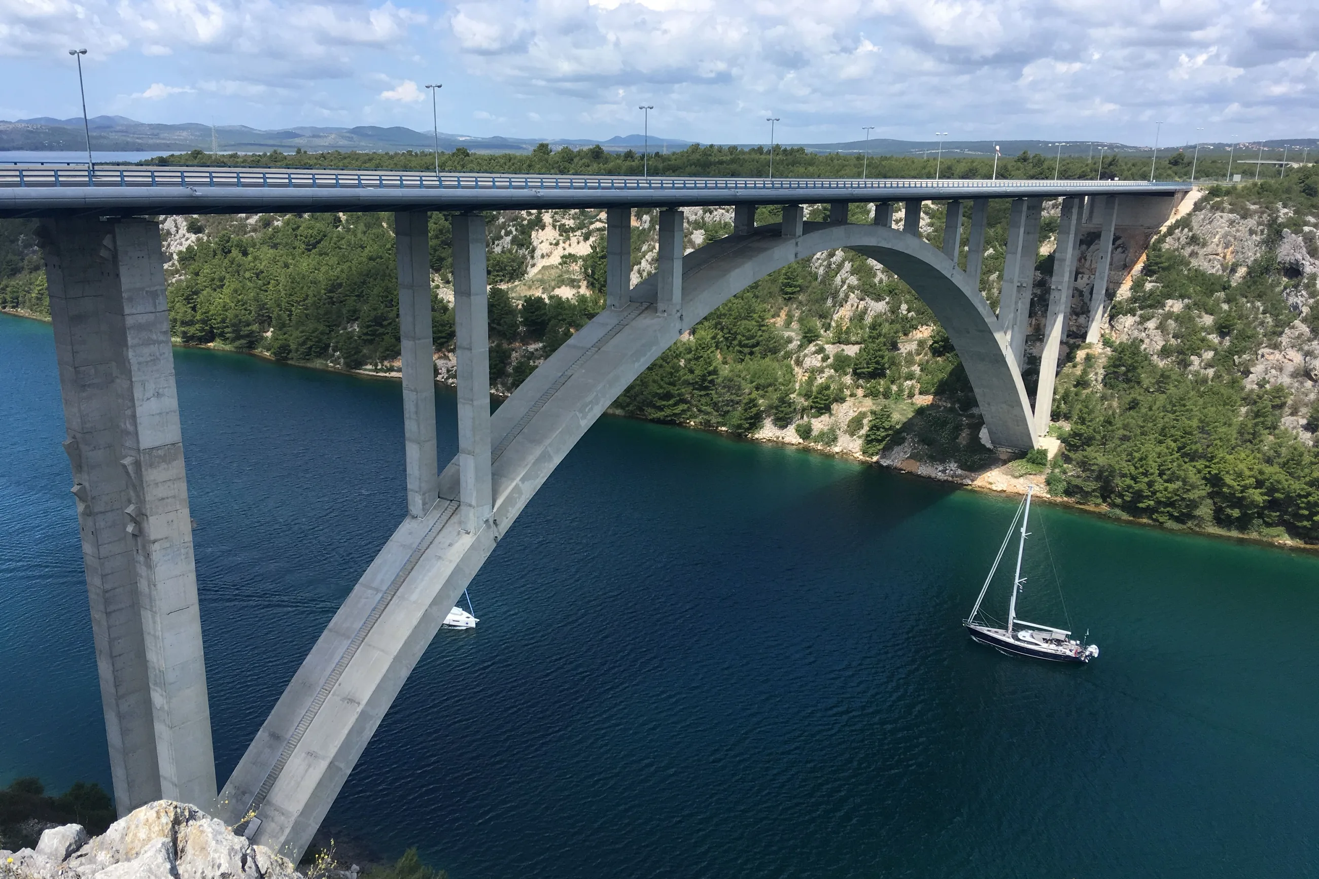 The Krka River Bridge near Šibenik: a concrete arch road bridge high above the river, with a sailing yacht on the water below